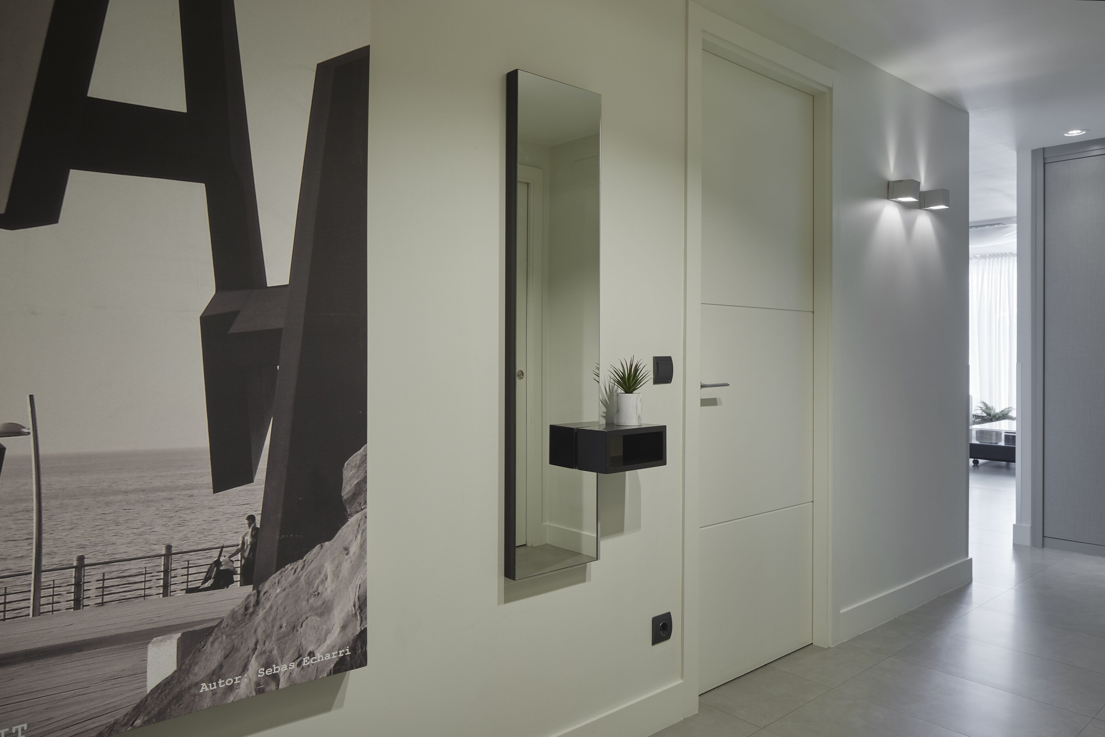 A modern hallway with a large abstract art piece, a mirror, and a small plant on a shelf.