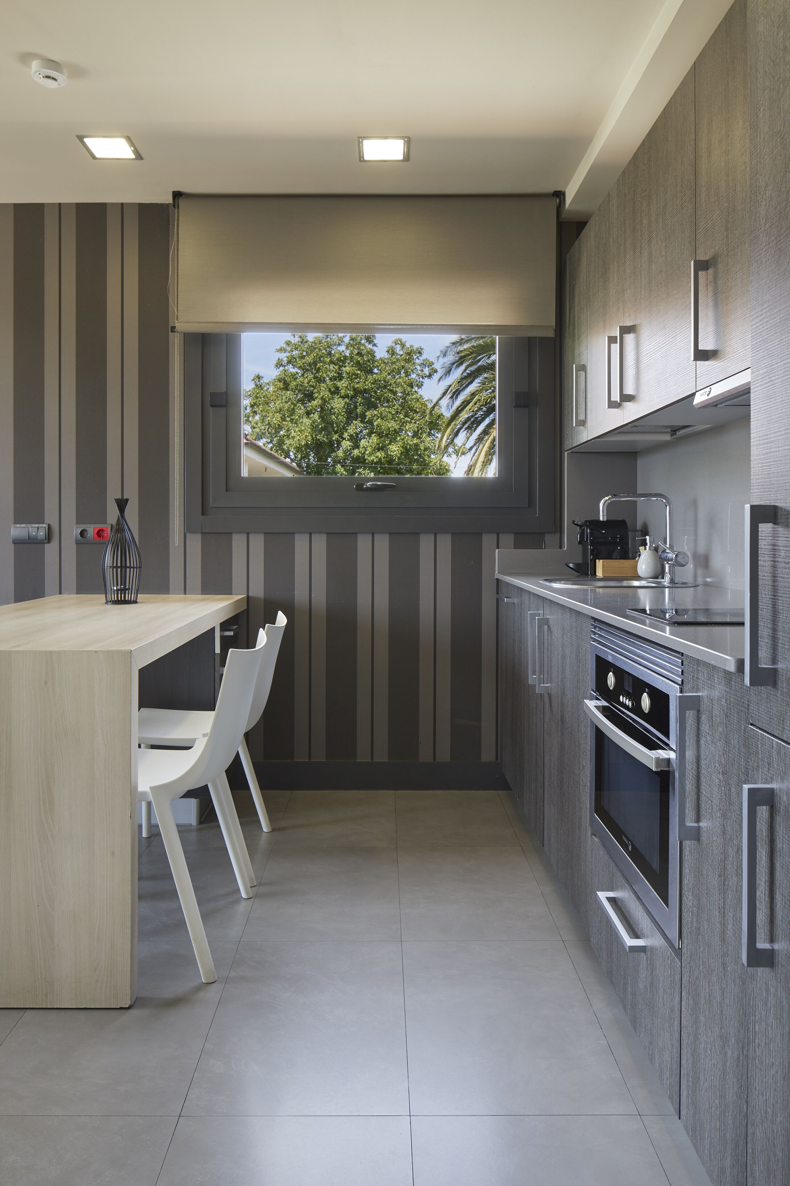 Una cocina moderna con una isla de madera, sillas blancas, un ventanal con vistas y electrodomésticos de acero inoxidable.