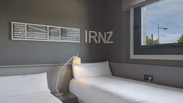 Een hotelkamer met twee eenpersoonsbedden, een nachtkastje met een lamp, een wanddecoratie en een raam met uitzicht.