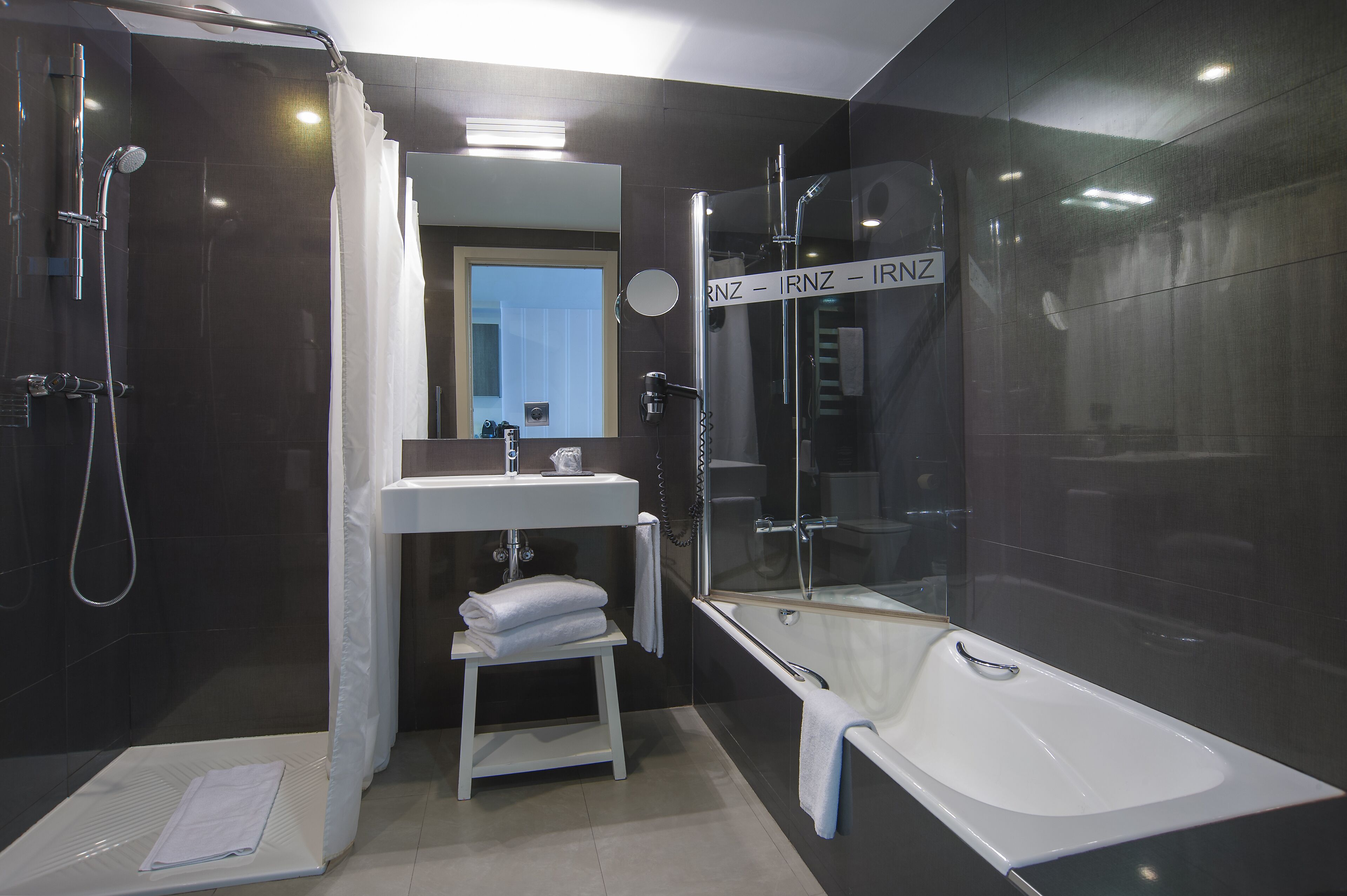 Een moderne badkamer met een douche met glazen wand, een wit wastafel en een bad.