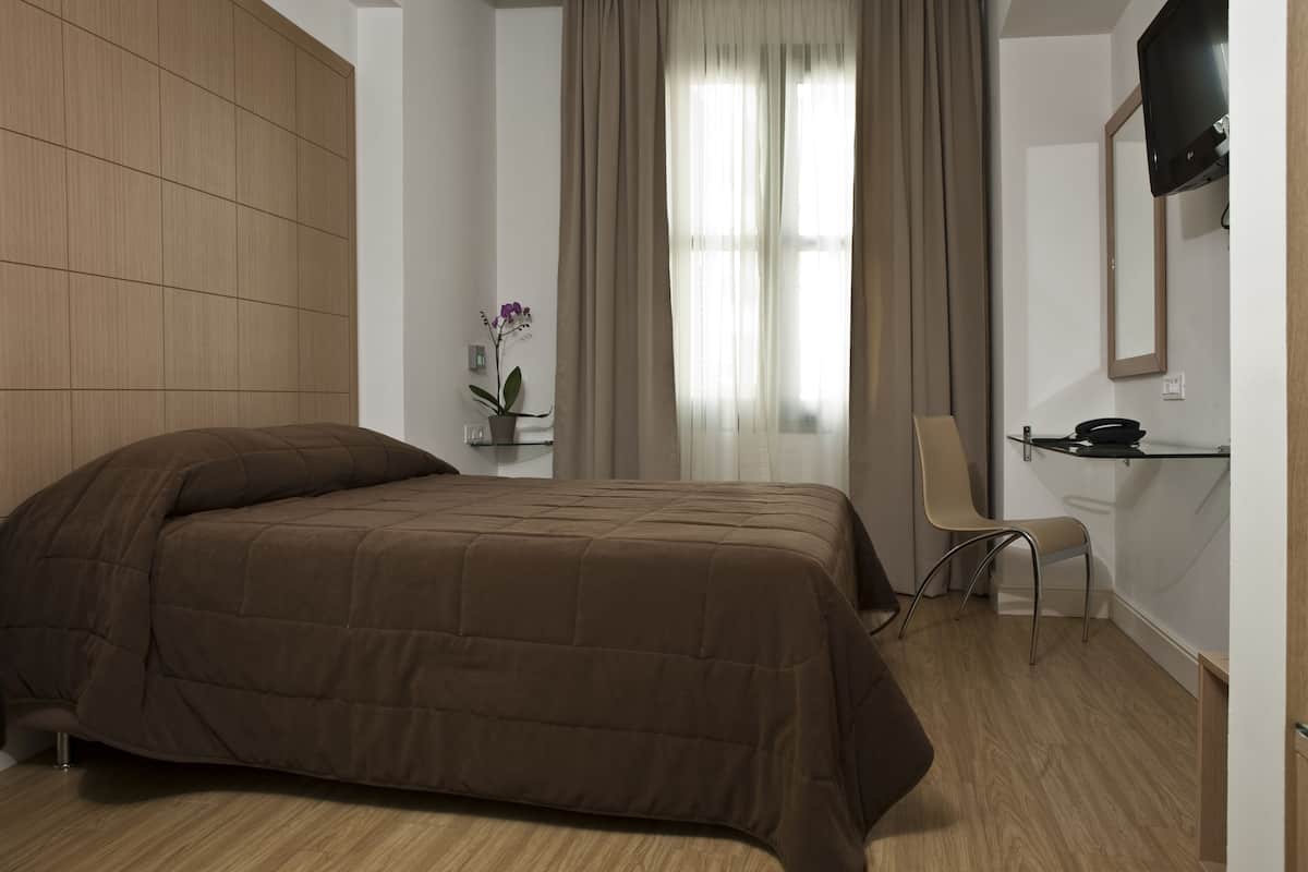 A modern bedroom with a large bed, a chair, a small table, and a TV mounted on the wall.