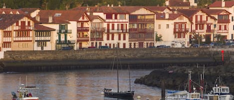 A coastal town with traditional timber-framed houses, a harbor with several boats, and a rocky breakwater.