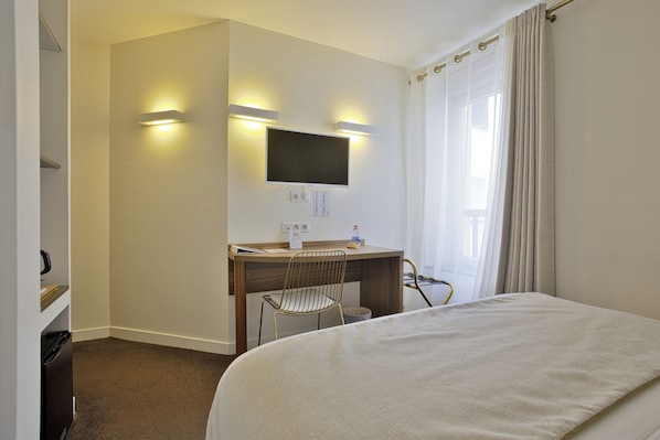 Een hotelkamer met een bed, een bureau met stoel, een televisie en een raam met gordijnen.