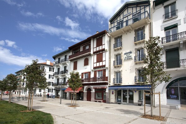 A row of hotels with balconies, a clear sky, and a sidewalk with trees. - Hôtel Le Relais Saint Jacques (Saint-Jean-de-Luz)