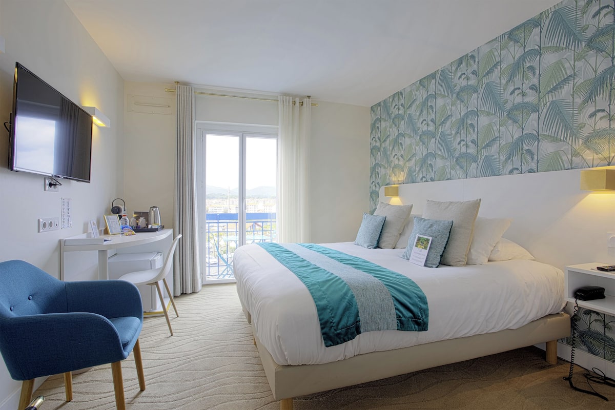 A hotel room with a bed, a desk, a chair, a TV, and a balcony with a view.