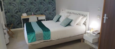 A neatly arranged bedroom with a bed, bedside table, lamp, and a desk with a chair.