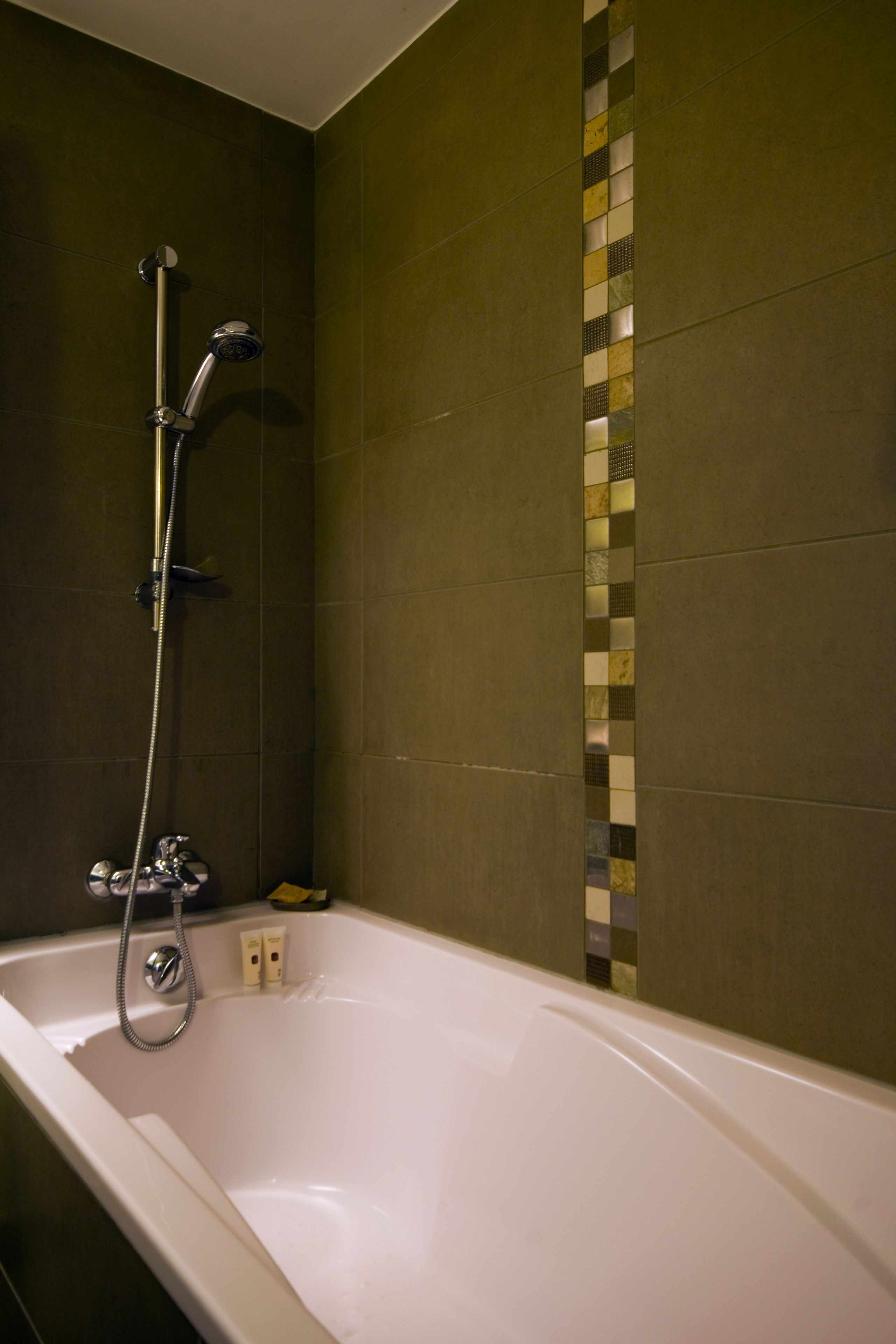 A bathroom with a bathtub, a shower, and a tiled wall with a decorative strip.