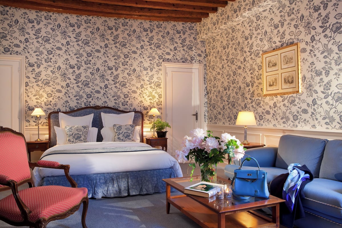 A bedroom with a bed, a chair, a sofa, a coffee table, and a wall with floral wallpaper.