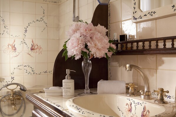 Ein Badezimmer mit Waschbecken, Spiegel, Blumen in einer Vase, einer Lotionflasche und einem Handtuch.