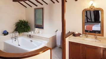 Une salle de bain avec une grande baignoire, un meuble-lavabo en bois, un miroir et une plante en pot.