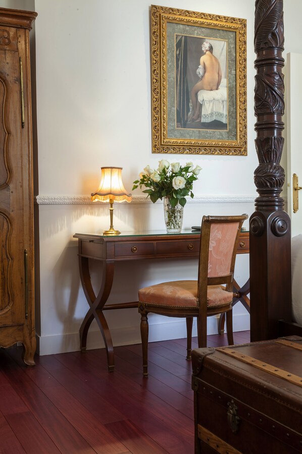 Ein Holztisch mit Lampe, ein Stuhl, eine Vase mit Blumen und ein Gemälde an der Wand.