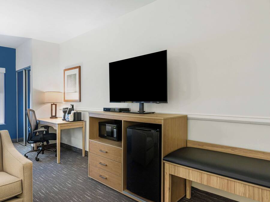 Una habitación de hotel con una cama, un escritorio con computadora, televisor, microondas y refrigerador.