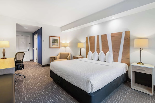A hotel room with a large bed, two bedside tables with lamps, a desk with a chair, and a framed picture on the wall. - Best Western Plus Westgate Inn & Suites (Leland)