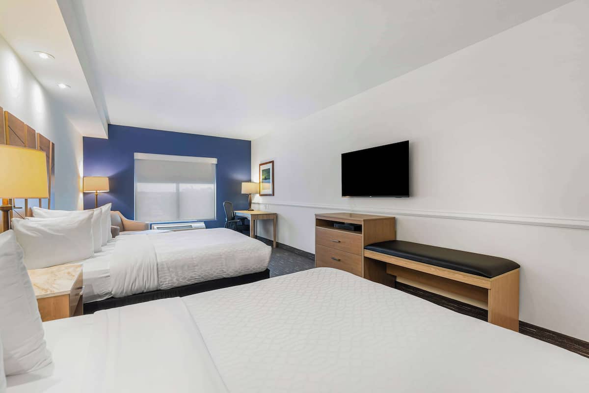 A hotel room with two beds, a desk, a chair, a TV, and a window.