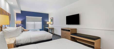 A hotel room with two beds, a desk, a chair, a TV, and a window.
