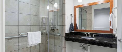 Ein modernes Badezimmer mit einer Duschkabine aus Glas, einem Waschtisch mit Waschbecken und Spiegel sowie einem Handtuchhalter.