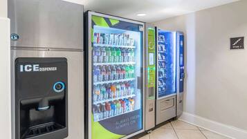 A row of vending machines in a hallway, including an ice dispenser and various beverage options.