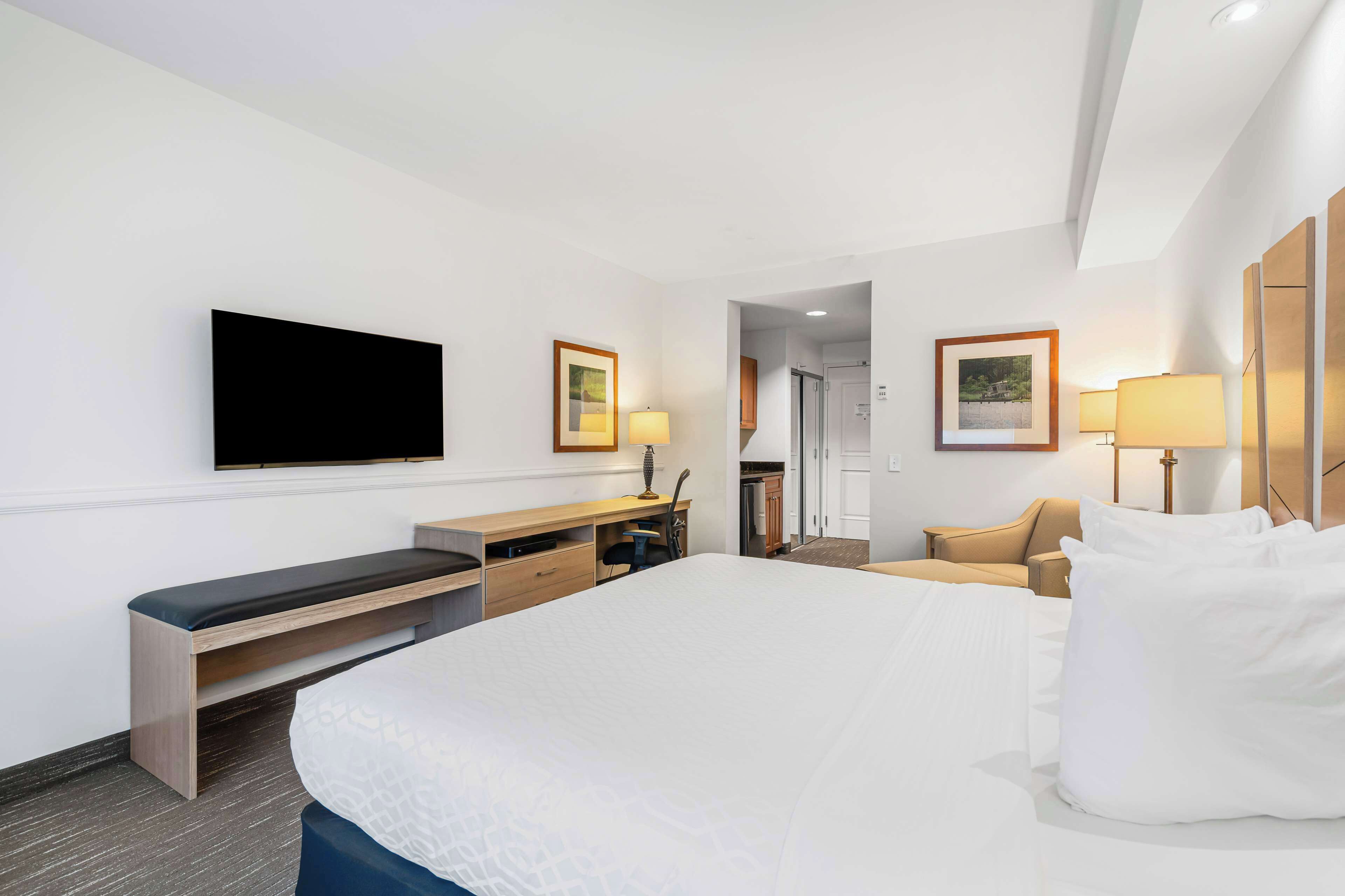 A hotel room with a large bed, a desk with a chair, a television, and a door leading to a bathroom.