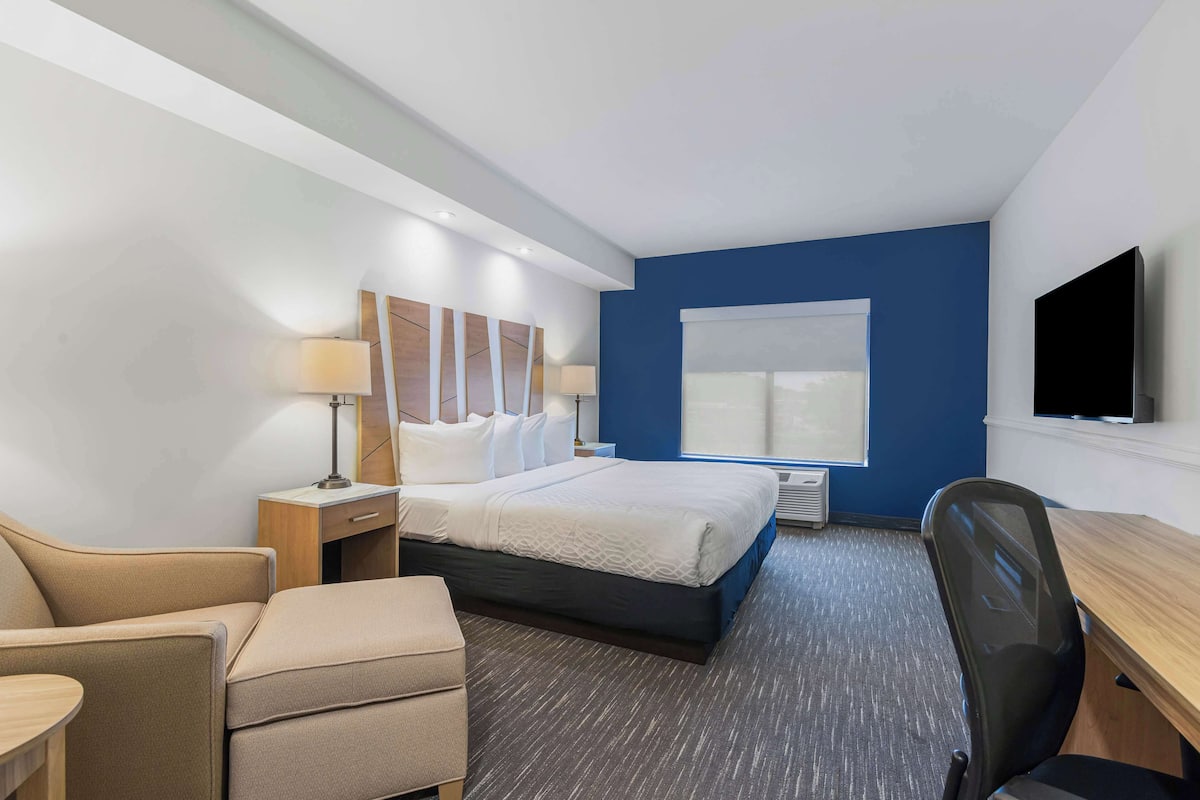 A hotel room with a bed, a desk, a chair, a lamp, and a TV.