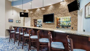 Una zona de bar con pared de piedra, varios taburetes, un televisor de pantalla plana y barra provista de botellas.