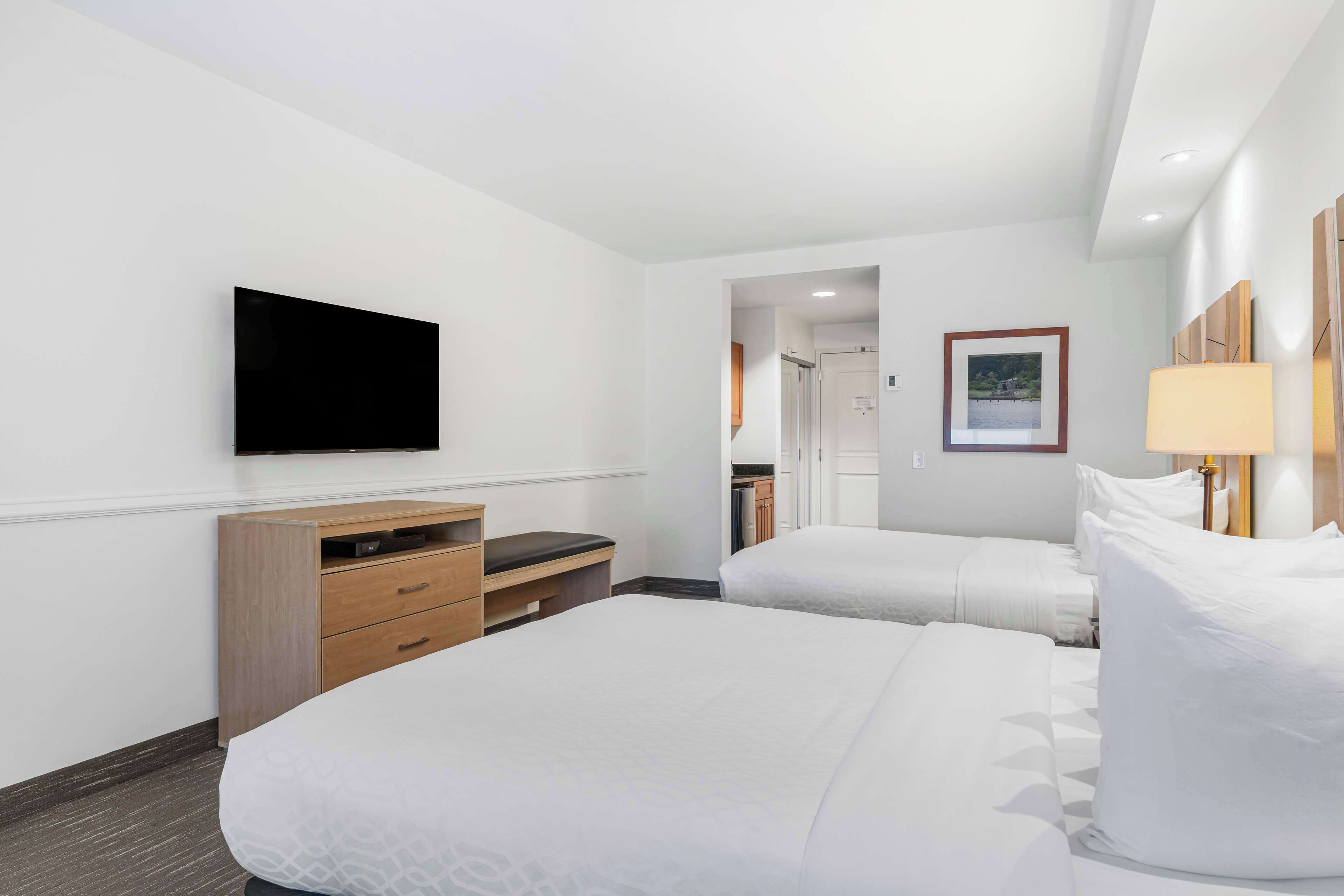 A hotel room with two beds, a flat-screen TV mounted on the wall, a wooden dresser, and a bedside lamp.