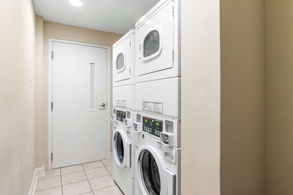 A laundry room with two stacked front-loading washers and dryers, a white door, and a tiled floor.