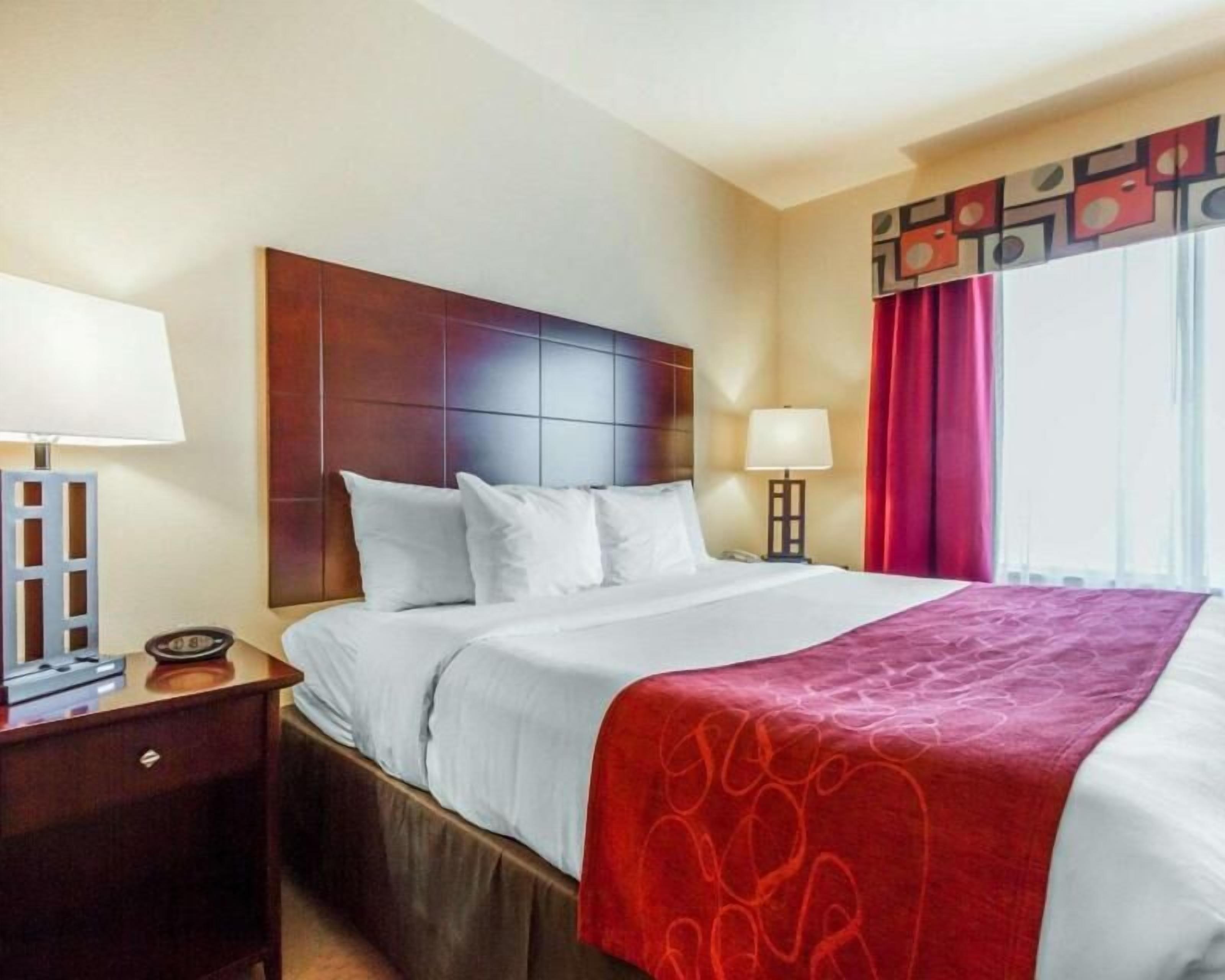 A hotel room with a bed, a nightstand, a lamp, a telephone, and a window with curtains.