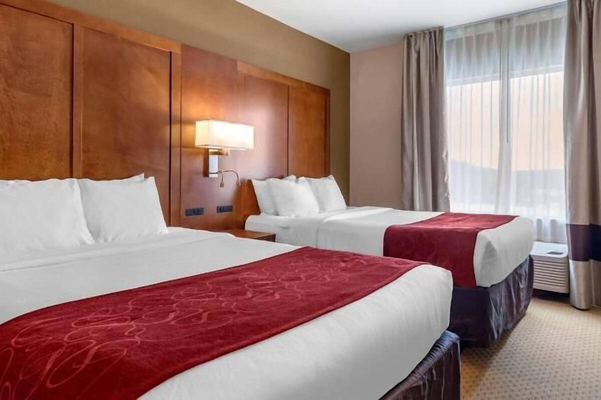 Ein Hotelzimmer mit zwei Betten, einem hölzernen Kopfteil, einer Wandlampe und einem fenster mit Vorhängen.