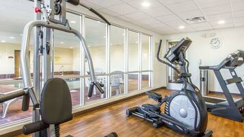 A gym with cardio machines, a weight bench, and a mirrored wall.
