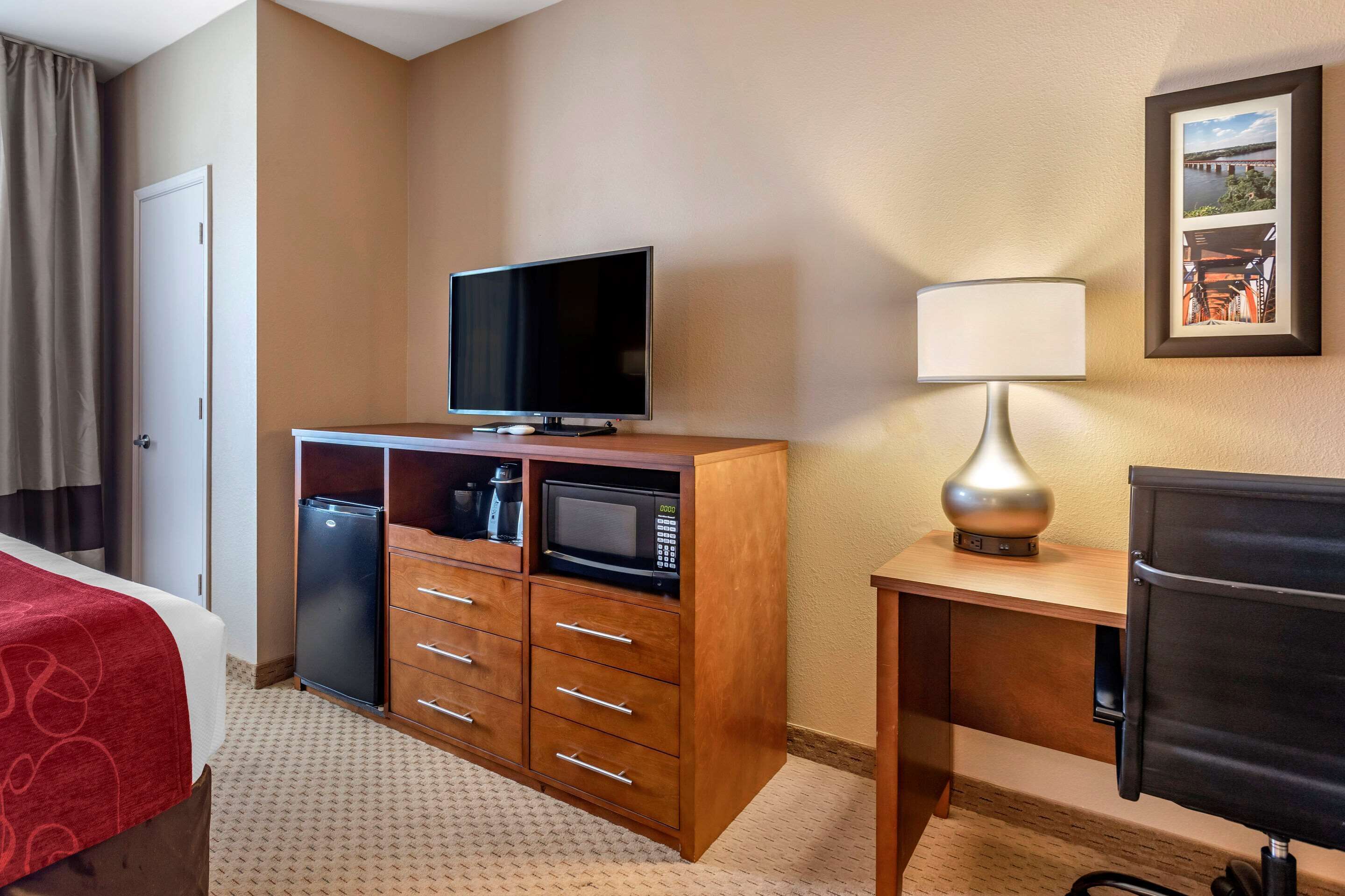 Habitación de hotel con cama, televisión, refrigerador, microondas, escritorio con lámpara y una silla.