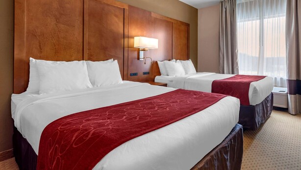 A hotel room with two beds, a wooden headboard, a wall-mounted lamp, and a window with curtains. - Comfort Suites Florence Shoals Area (Florence)