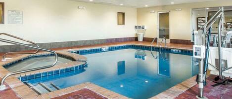 An indoor swimming pool with a red-tiled floor, clear blue water, and metal handrails.