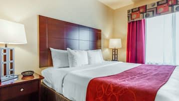 A hotel room with a large bed, a wooden headboard, a nightstand with a lamp, and a window with red curtains.
