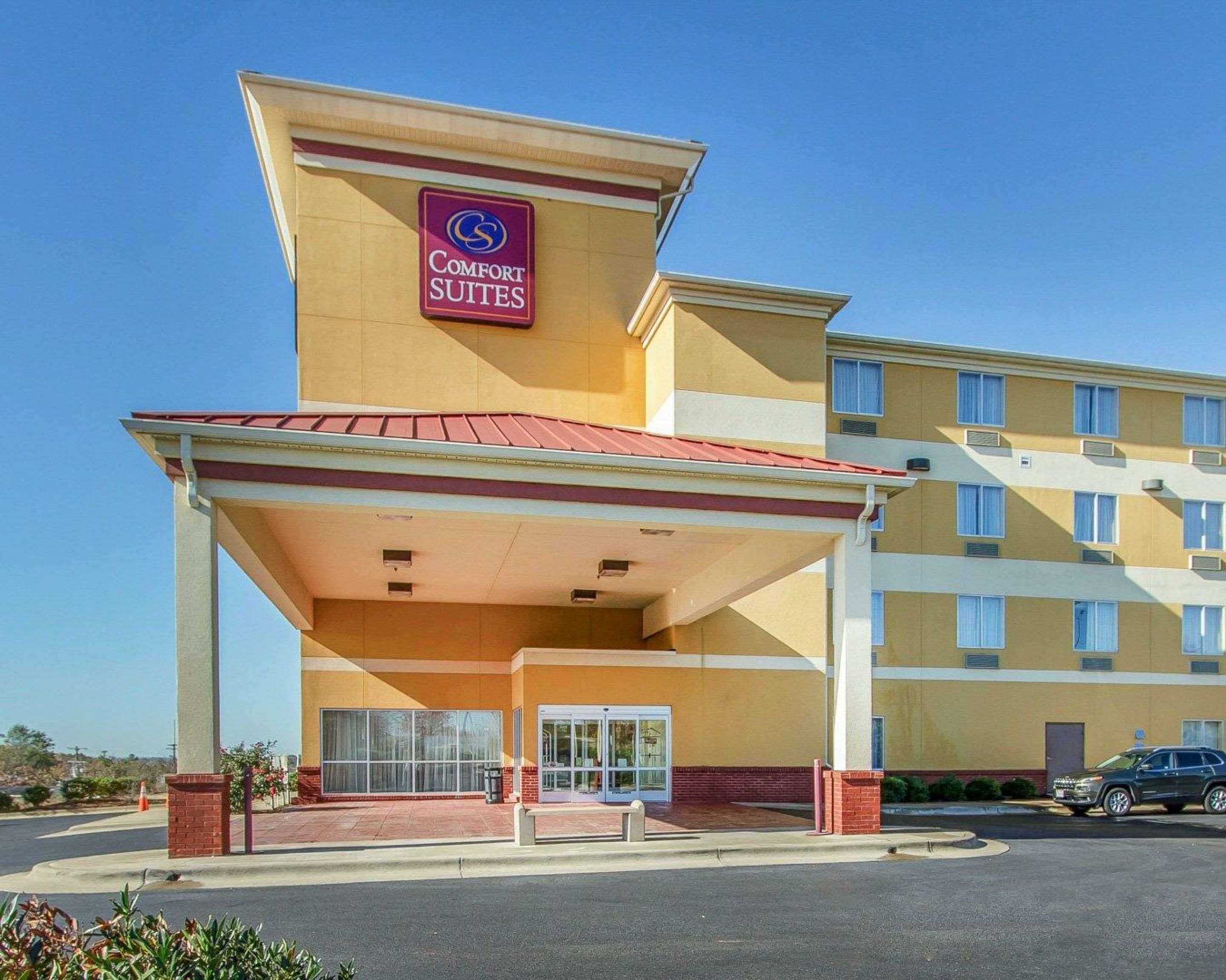 Um hotel Comfort Suites com entrada coberta, estacionamento e céu azul.
