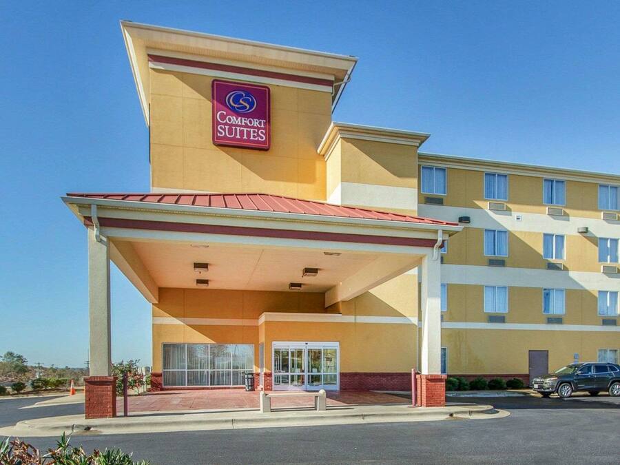 Um hotel Comfort Suites com entrada coberta, estacionamento e céu azul.