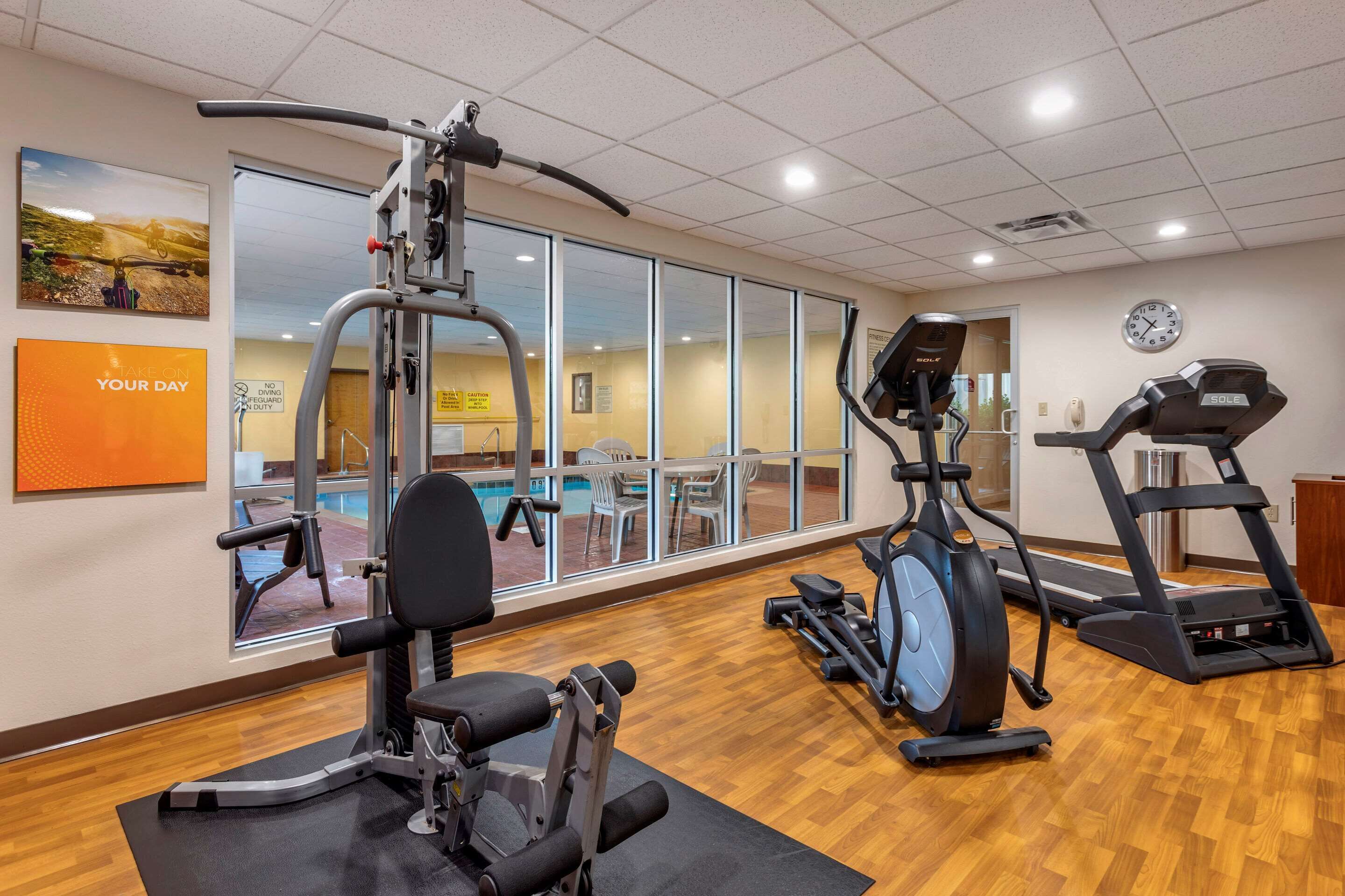 A gym with cardio machines, a weight bench, and a pool visible through large windows.