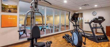 A gym with cardio machines, a weight bench, and a pool visible through large windows.