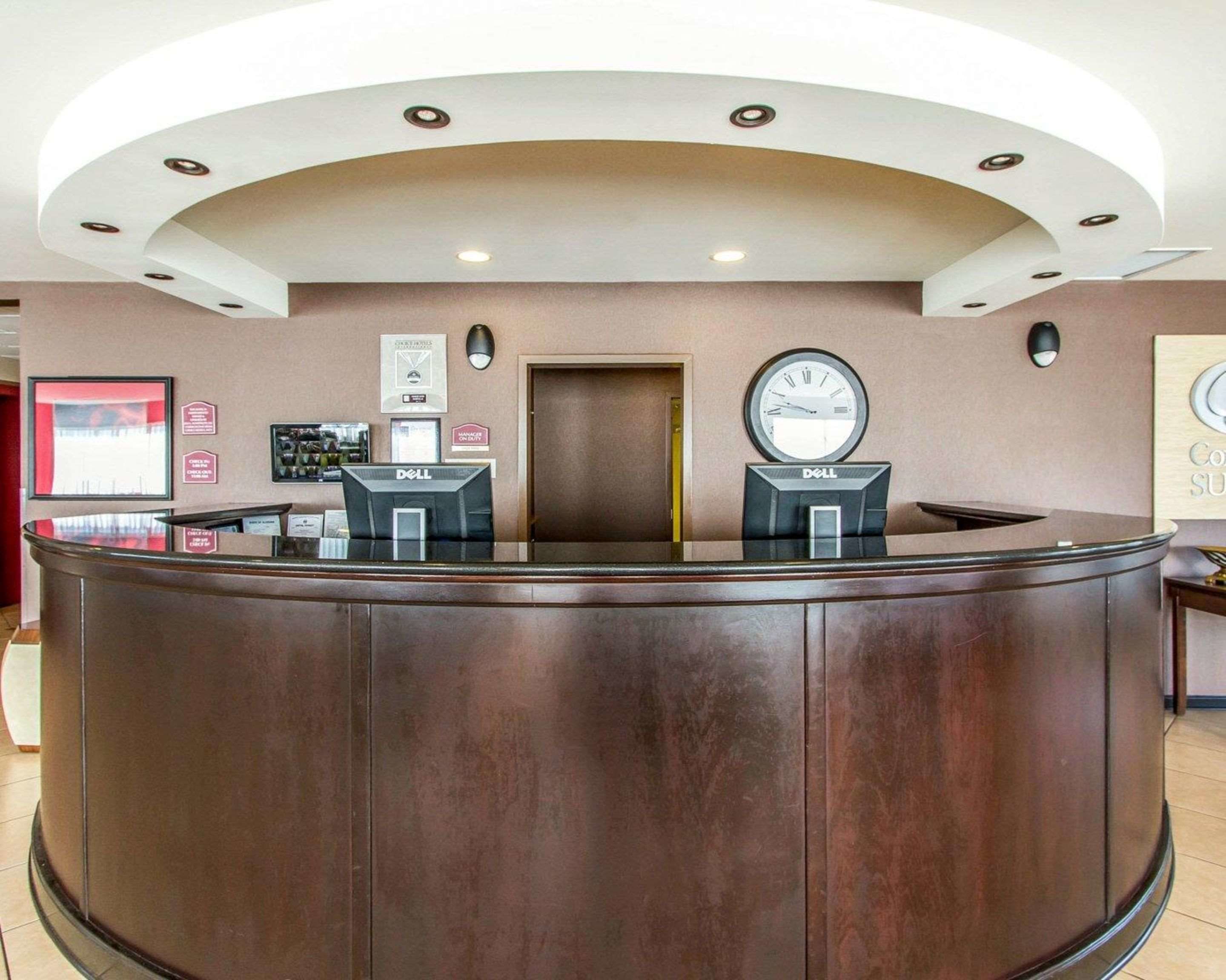 A reception desk with a curved design, two computer monitors, a clock, and a framed picture on the wall.