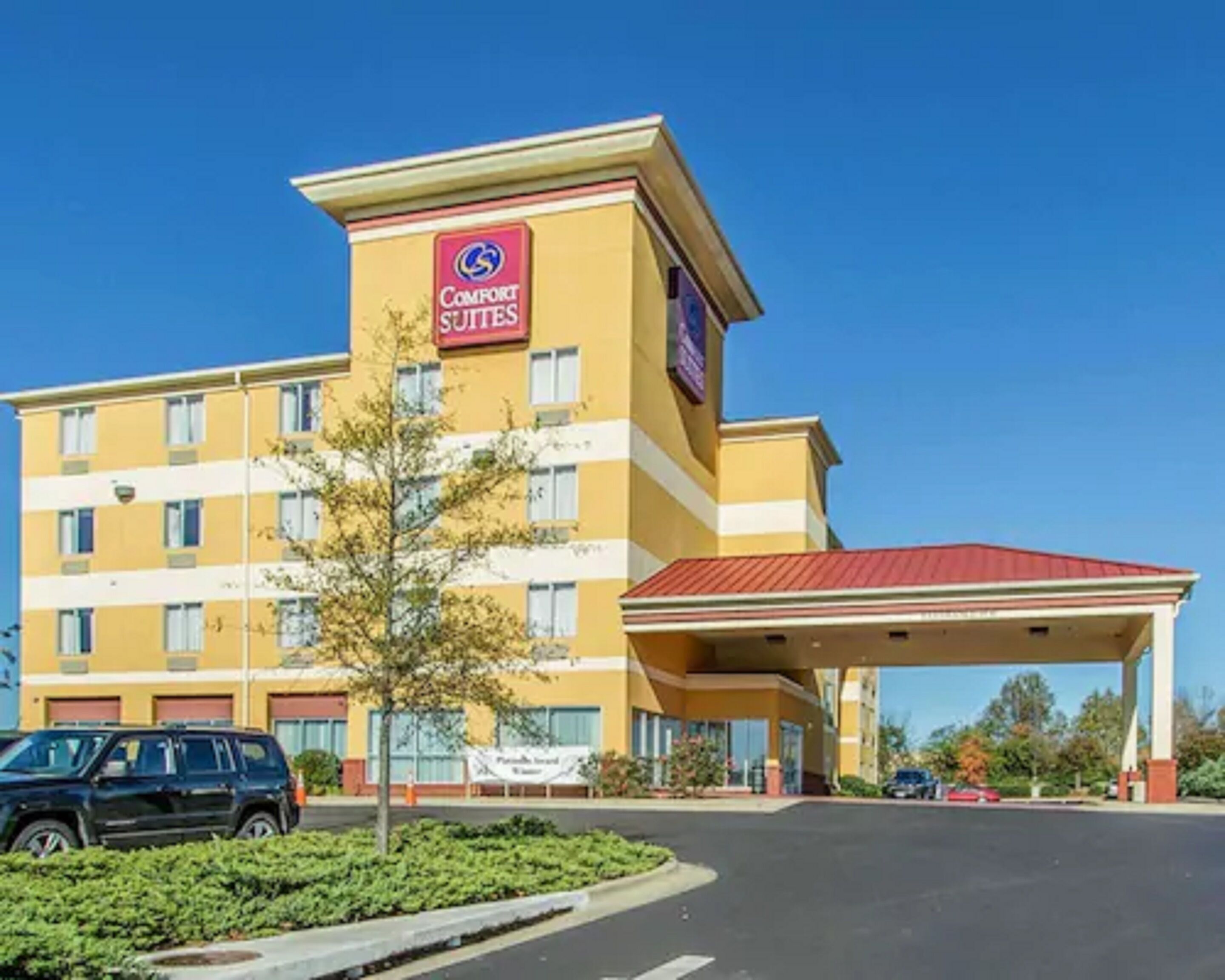 Un hôtel Comfort Suites avec une façade jaune, un toit rouge et un espace de stationnement couvert.
