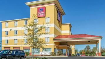 Um hotel Comfort Suites com fachada amarela, telhado vermelho e área de estacionamento coberta.