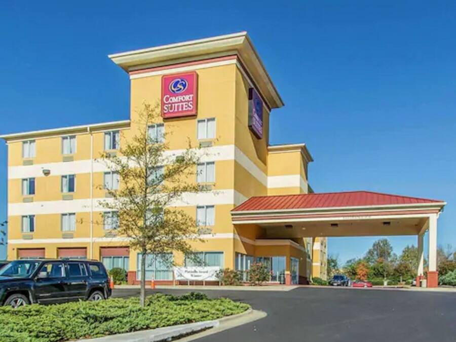 Um hotel Comfort Suites com fachada amarela, telhado vermelho e área de estacionamento coberta.