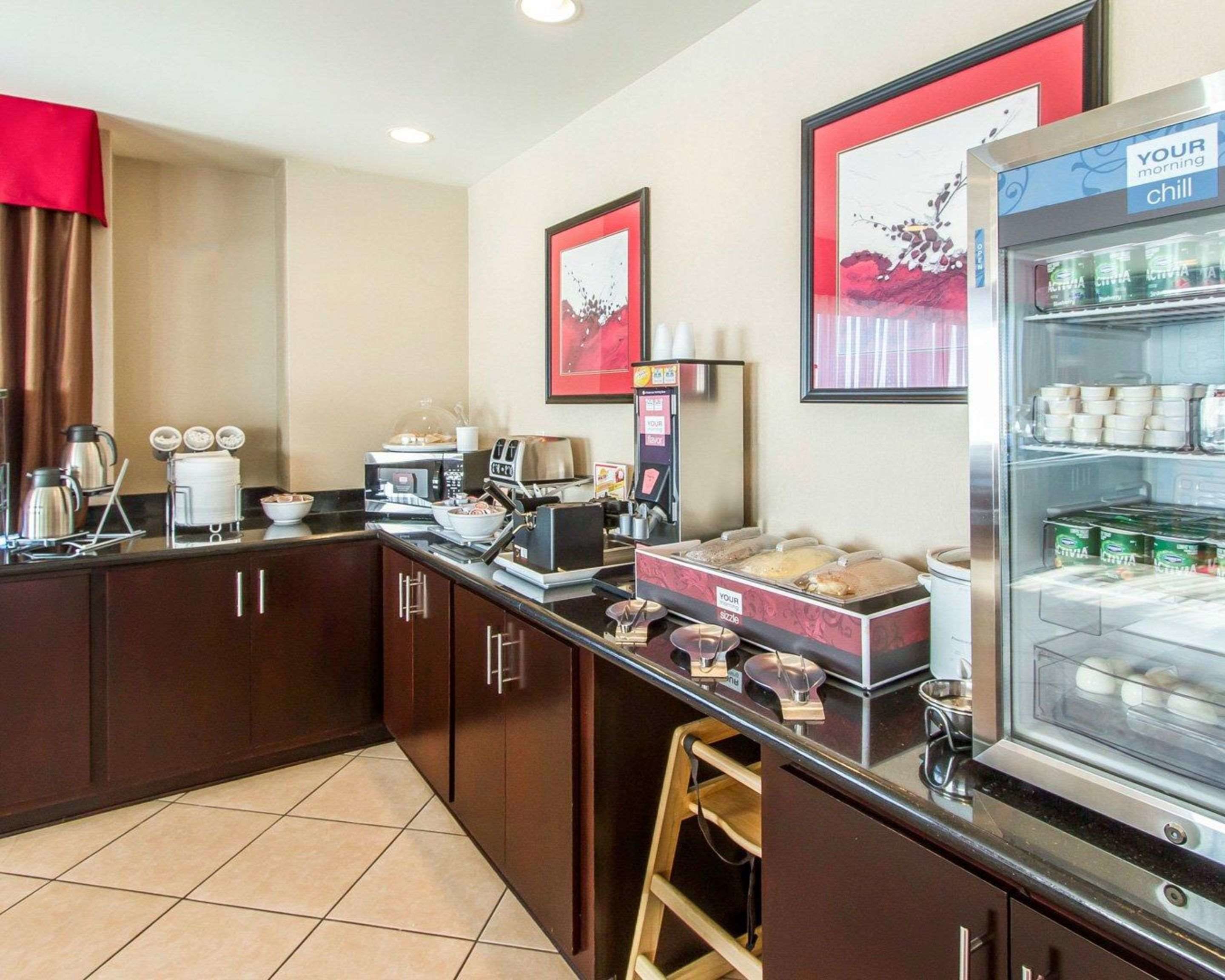A breakfast bar with coffee machines, a refrigerator with beverages, and a framed picture on the wall.