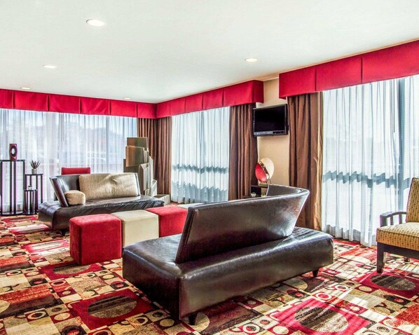 Habitación de hotel con un ventanal grande, un televisor de pantalla plana, un sofá, una silla y una alfombra estampada.
