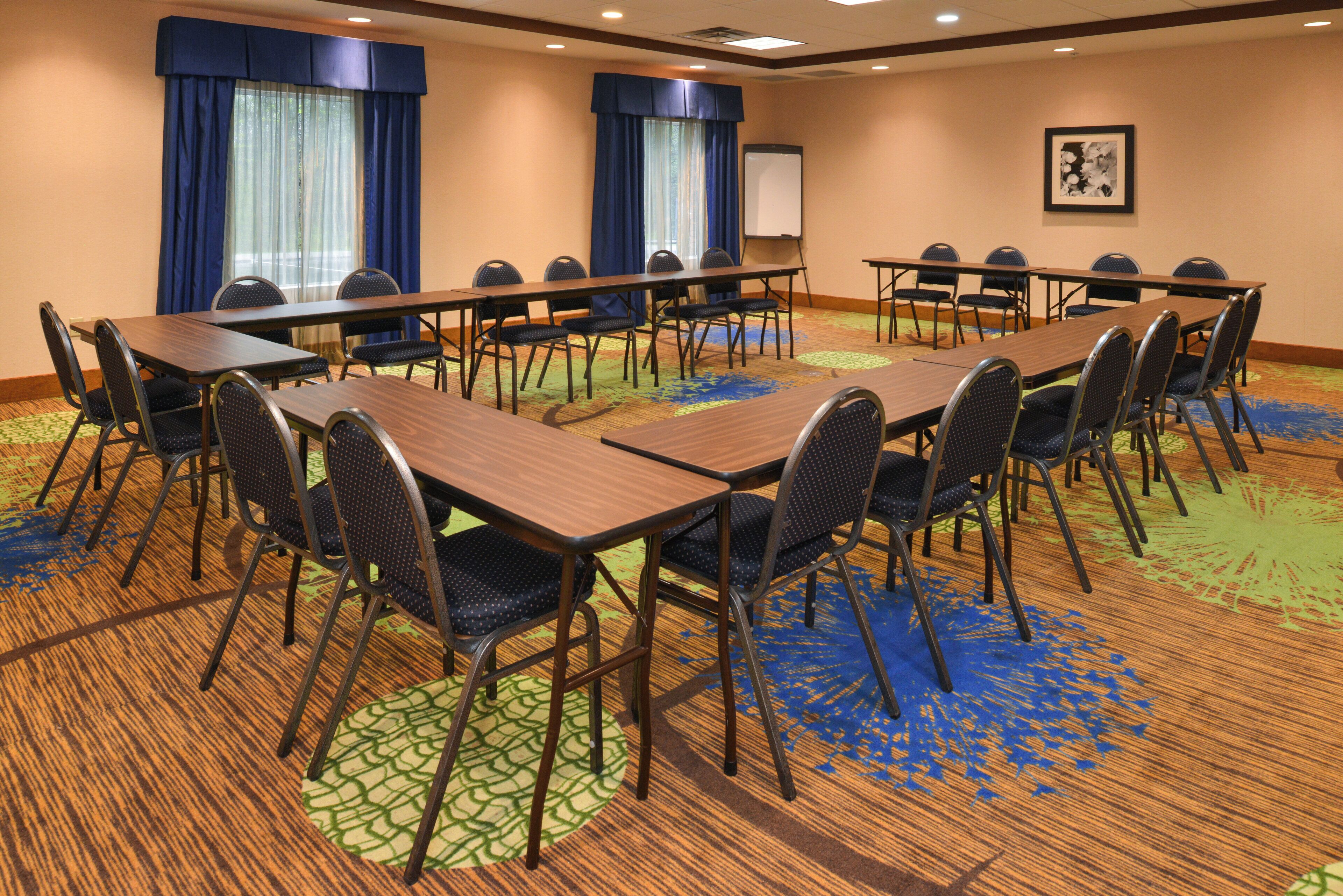 A conference room with multiple tables and chairs, a projector screen, and a carpeted floor.