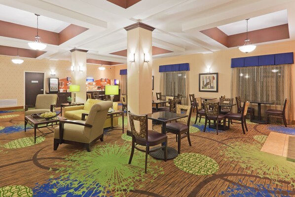A hotel lobby with multiple seating areas, including sofas and chairs, arranged around a central column. There are tables and a counter with a menu display. The lobby features a patterned carpet and ceiling with recessed lighting. - Holiday Inn Express Columbia by IHG (Columbia)