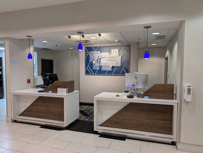 En receptionsområde med to diske, en blå væg med et Holiday Inn Express skilt, og et moderne loftdesign.