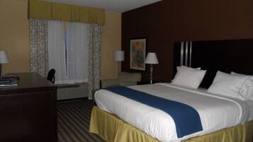 A hotel room with a large bed, a desk, two chairs, a lamp, and a painting on the wall.