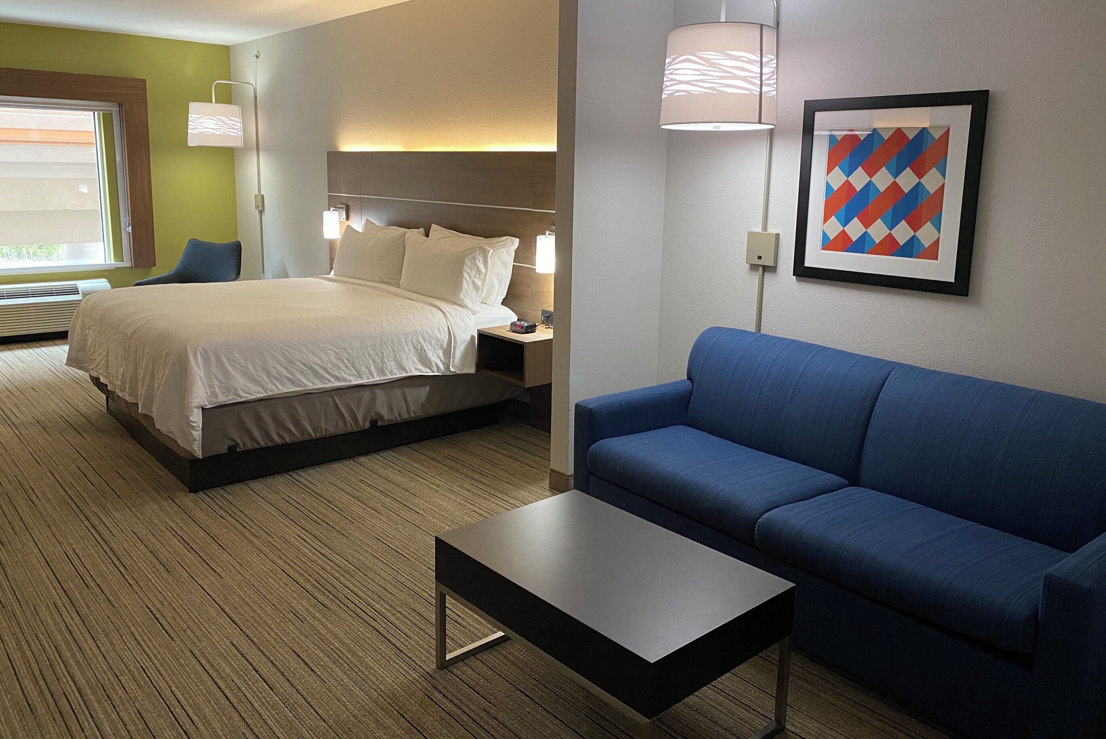 A hotel room with a bed, a blue sofa, a small table, and a framed picture on the wall.