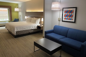 Une chambre d’hôtel avec un lit, un canapé bleu, une petite table et un tableau encadré au mur.