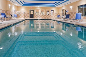 A swimming pool with clear water, surrounded by lounge chairs and a tiled wall with a checkered pattern.